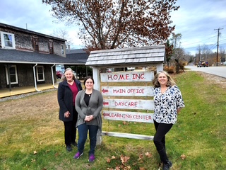 Three people standing next to the sign for H.O.M.E